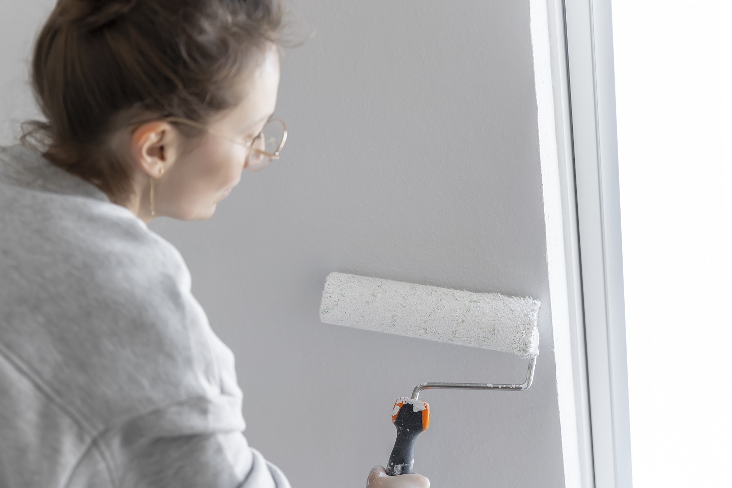 Kobieta maluje wałkiem ścianę na biało