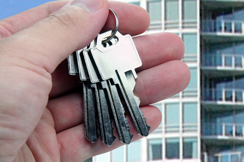 Dłoń trzymająca pęk kluczy, w tle nowoczesny apartamentowiec
