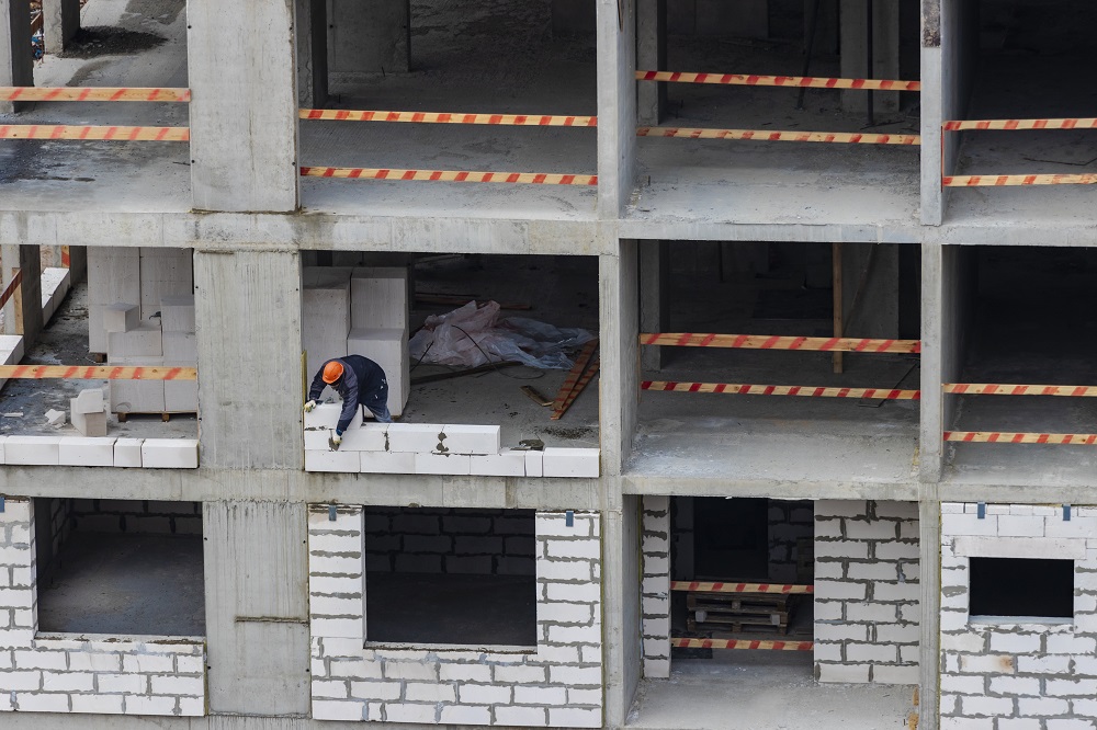 Front bloku mieszkalnego w trakcie budowy - widoczny robotnik murujący ścianę