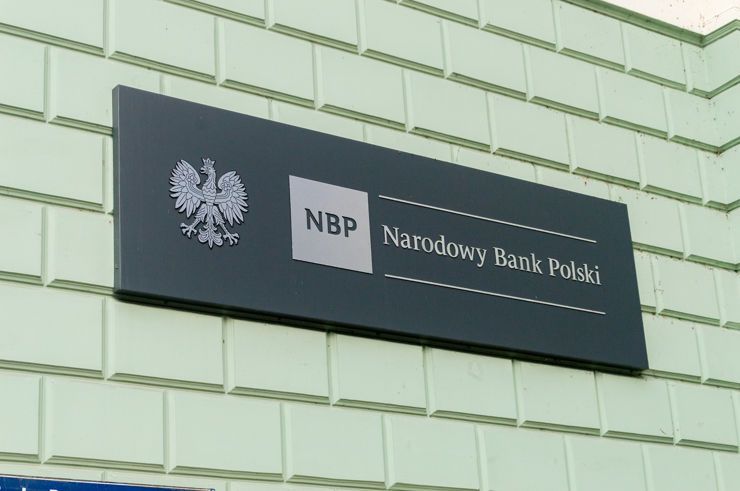 Tablica informacyjna na ścianie z godłem Polski (orzeł) oraz napisaem "NBP" i "Narodowy Bank Polski"