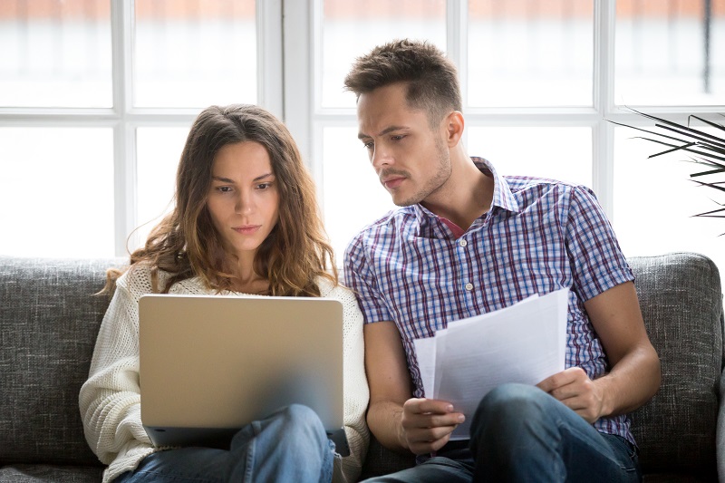 Kobieta i mężczyzna oglądają coś na laptopie, mężczyzna trzyma plik dokumentów