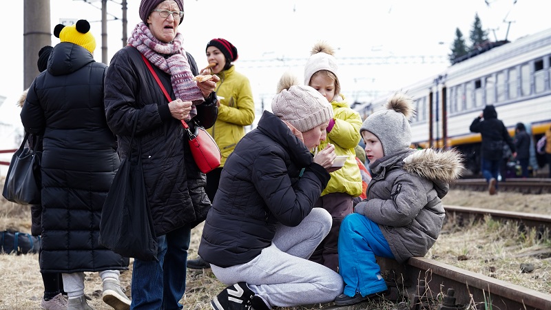 Grupa uchodźców siedzących na torach kolejowych