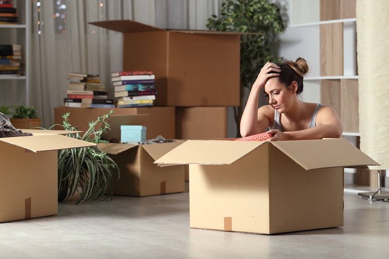 Zmartwiona kobieta siedzi na podłodze, otoczona pudełkami ze spakowanymi rzeczami